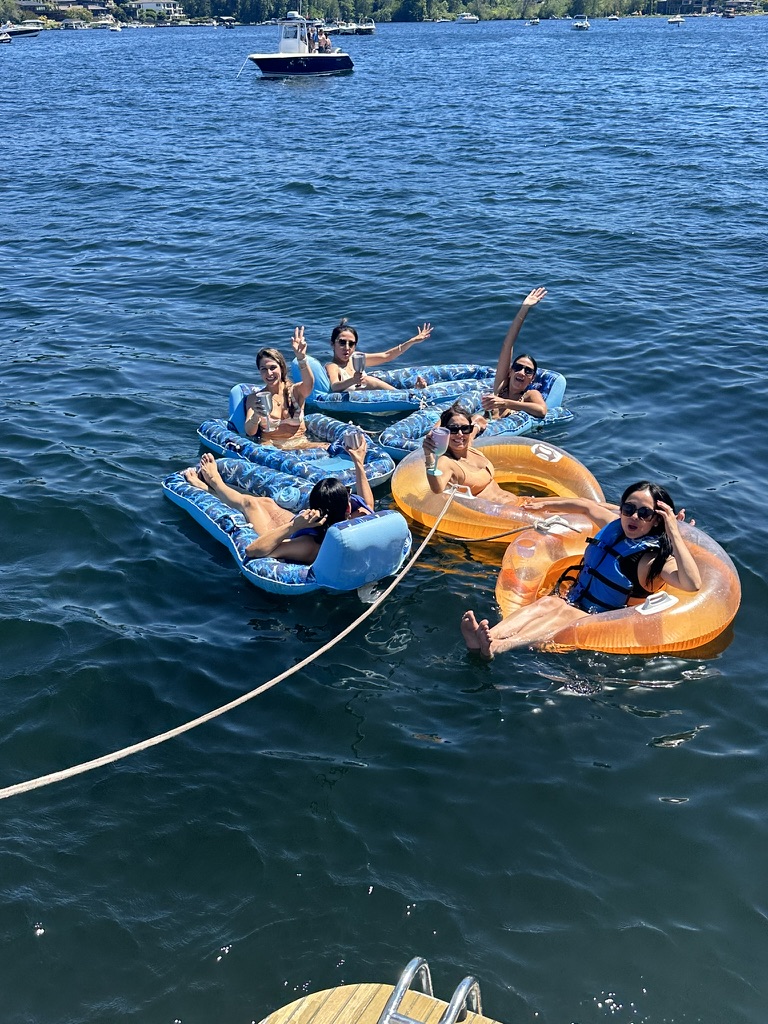 Guests relaxing on floaties tied off the boat on a sunny day on Lake Washington