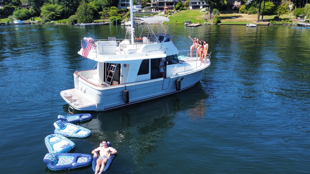 Modern flybridge yacht anchored on Lake Washington with guests on the bow and a swimmer on a floatie alongside